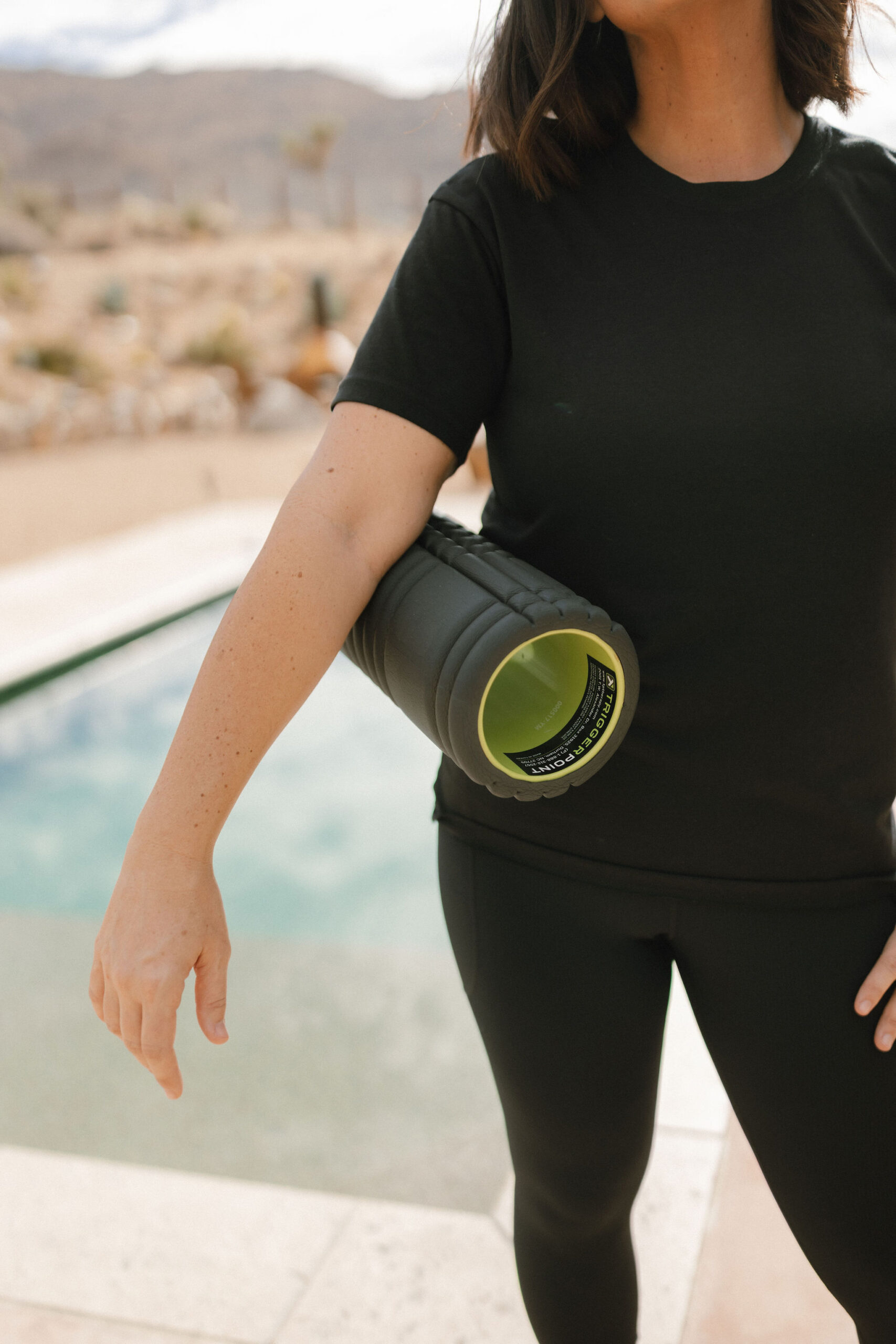 Massage therapist holding a foam roller outdoors, preparing to demonstrate proper foam rolling techniques.